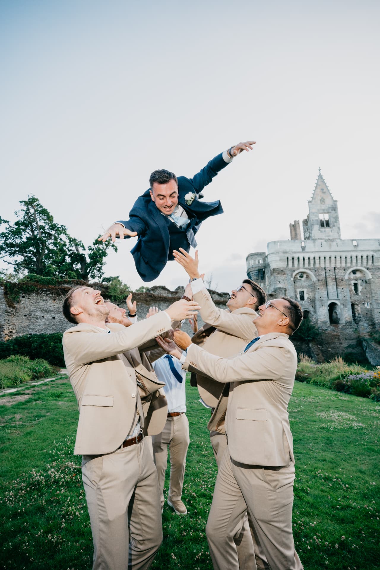 Le marié lancé en l'air par ses témoins devant un château, photo de mariage