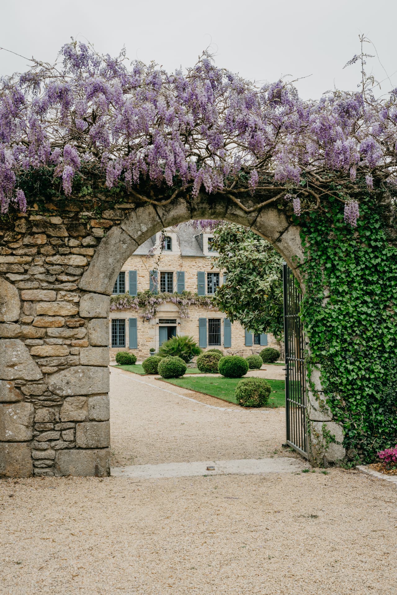 Portail de pierre couvert de glycines donnant sur un manoir
