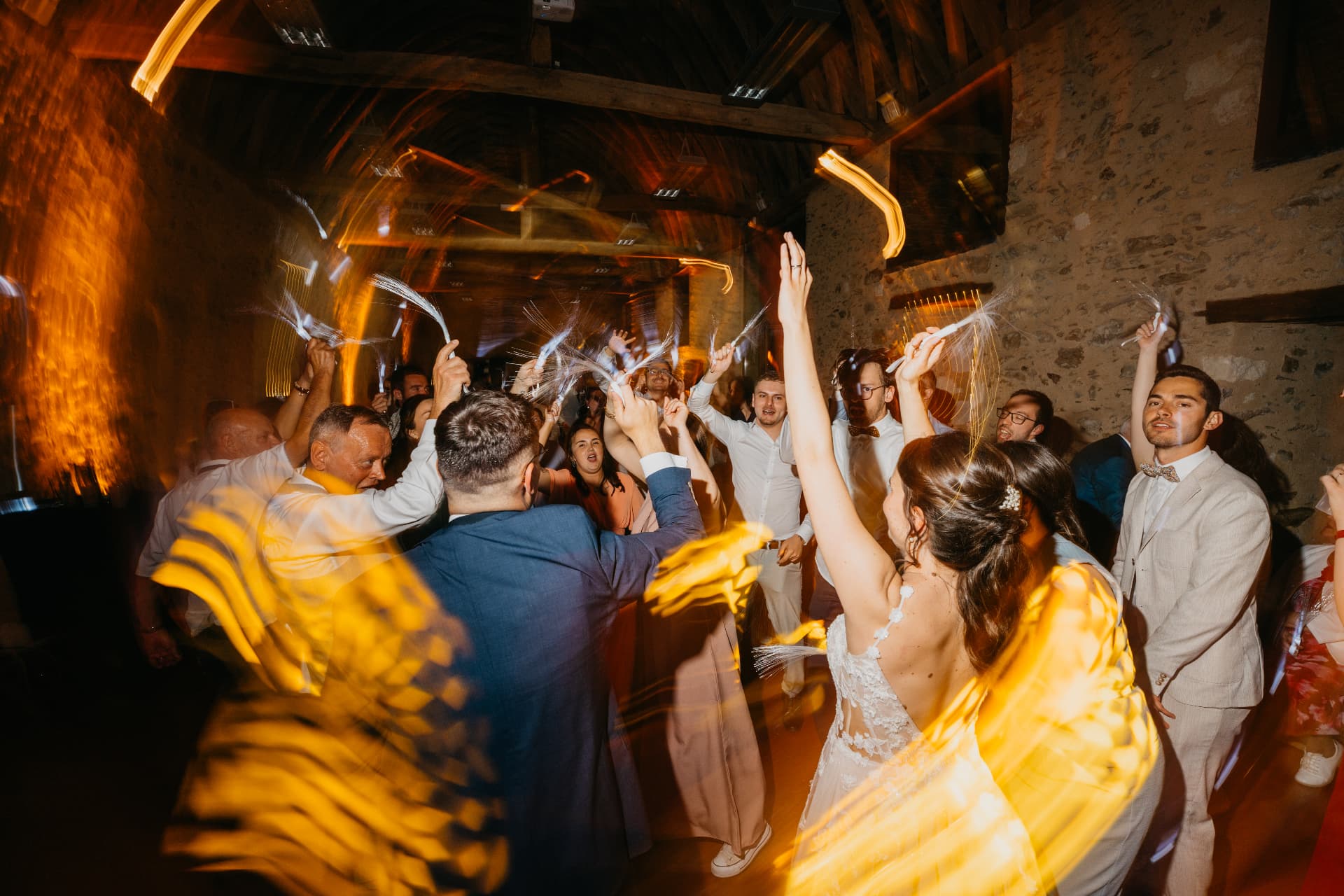 La mariée danse bras levés sous les traînées de lumière de la salle