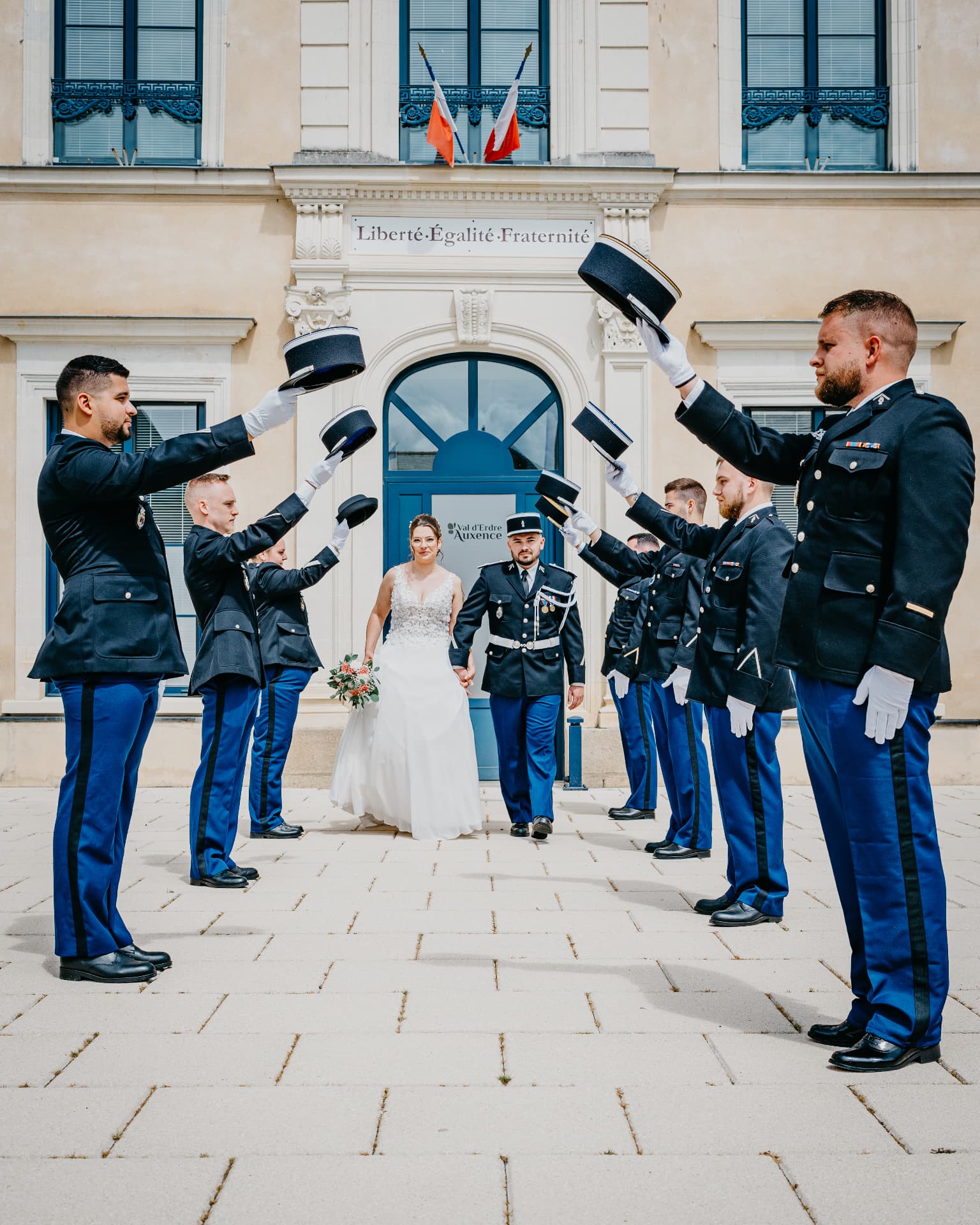Les mariés passent sous une haie d'honneur de gendarmes levant le képi devant une mairie