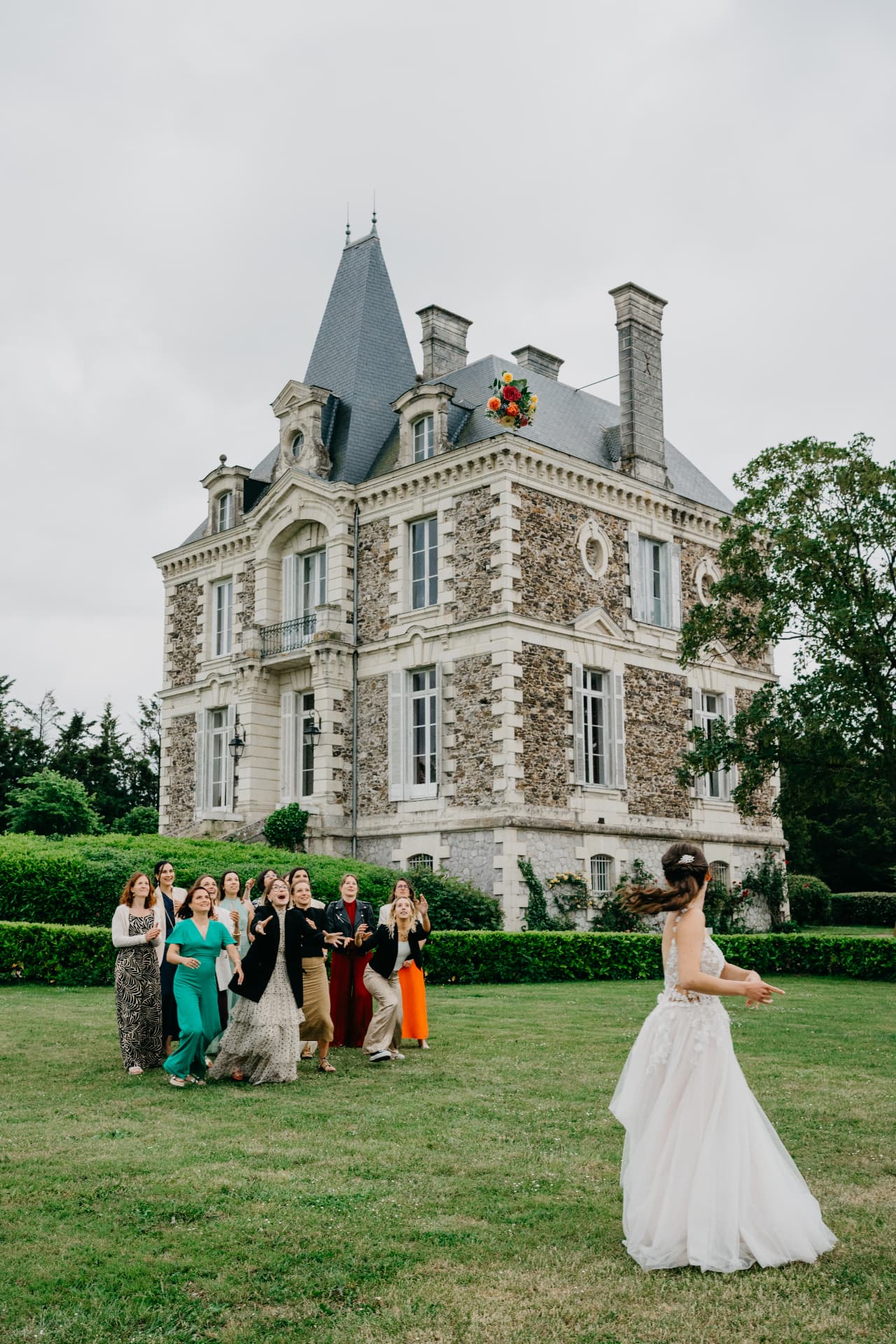 La mariée lance son bouquet devant le château, les invitées prêtes à le rattraper