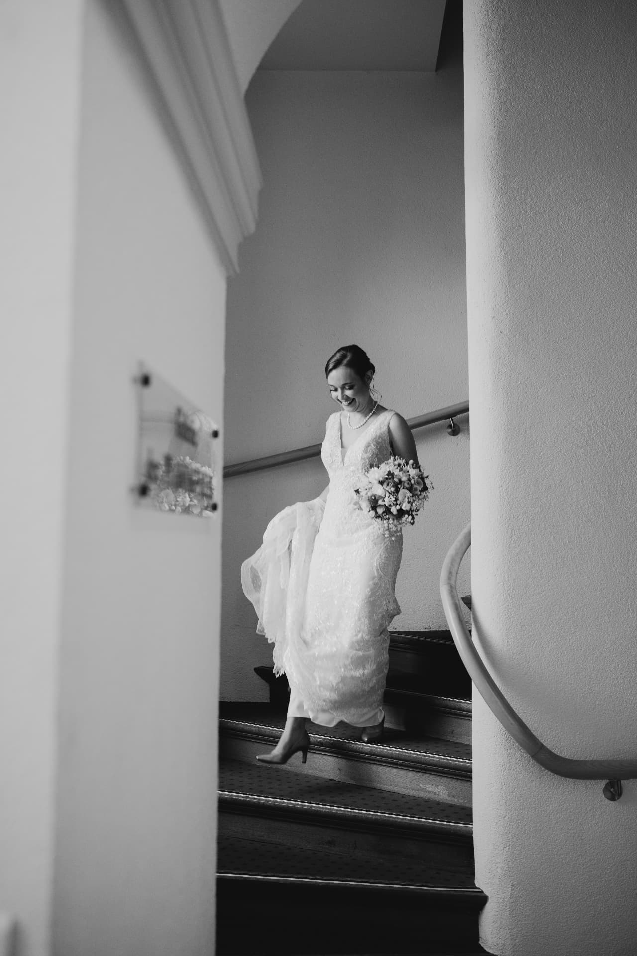 La mariée en robe blanche descend un escalier, bouquet en main