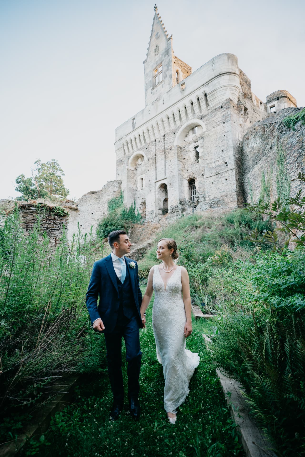 Les mariés avancent main dans la main dans un jardin devant le donjon d'un château